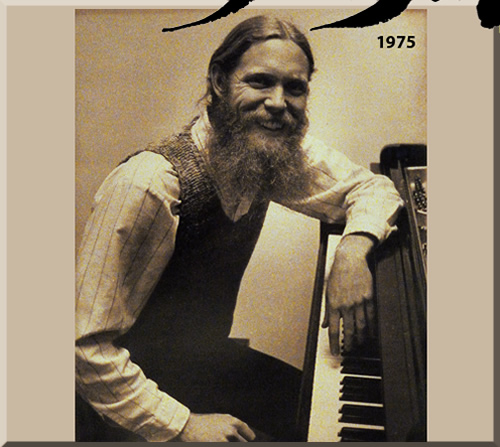 Nineteen seventy-five photo of Jerry Michelsen seated at a grand piano. He's sporting long, blond hair and a long red beard.