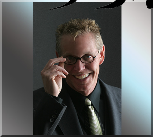 Photo of Jerry Michelsen smiling in a grey suit with his hand near his glasses, ready to remove them